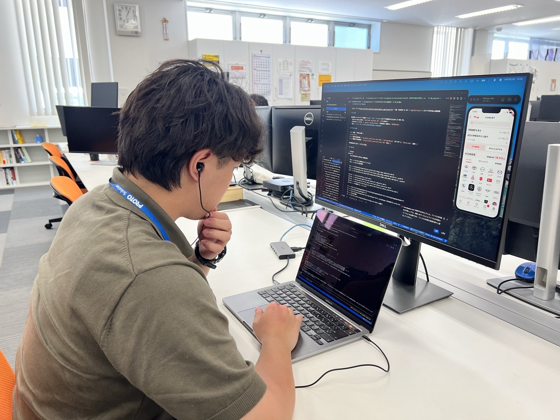 アプリ画面とコードを表示したモニターの前で開発する杉浦さん